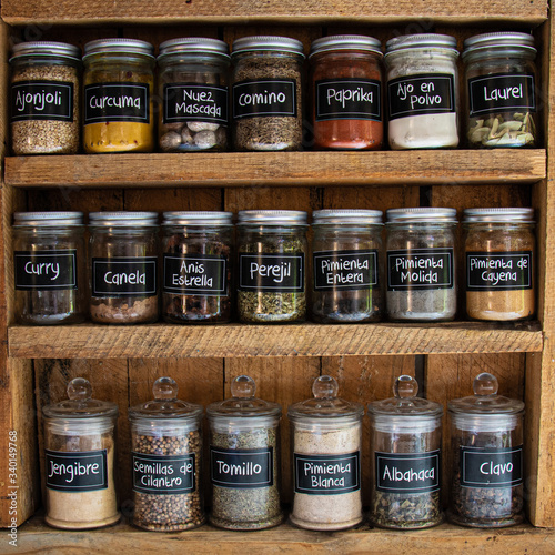 Glass reusable spice jars in a rustic wooden cabinet with spice names written in spanish