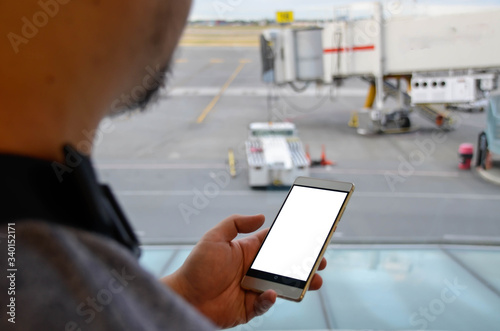 POV of an asian man while holding using a smartphone a mobile smart phone in airport terminal building in summer daytime. Business man while holiday.. Looking at smartphone.