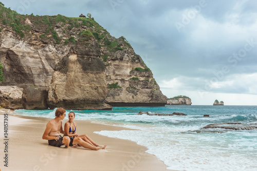 girl and a Man sit on a Diamond beach on the island of Nusa Penida.