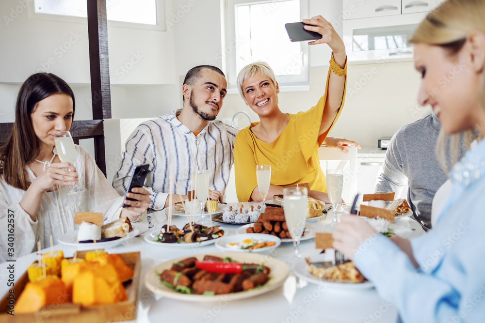 Group of multicultural friends having healthy lunch at home. Two of them taking selfie.