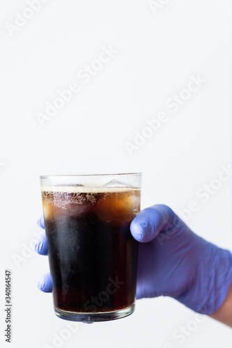 human hand with protective glove holding a glass of cola. Concept for celebrating the end of the coronavirus crisis, covid 19