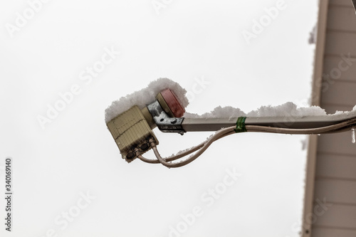 A snow-covered converter of a satellite dish against a grey sky close-up.