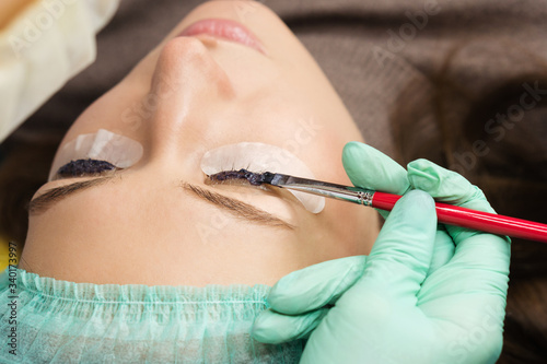 Beauty treatment. Cosmetologist puts black paint on the lashes. Laminating eyelashes. Closeup eyes.