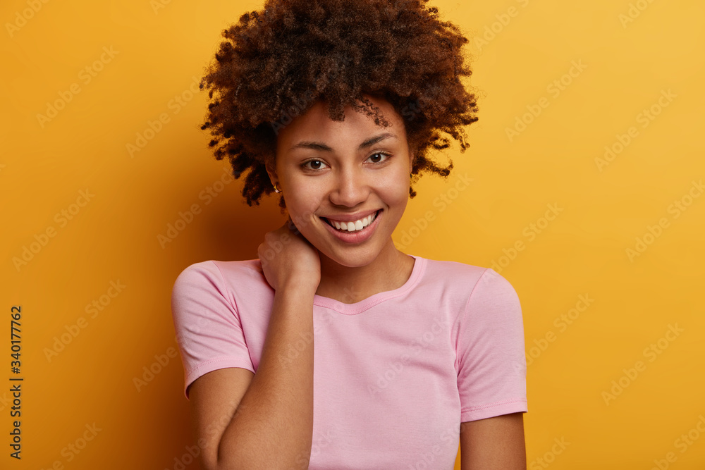 Portrait of happy Afro American woman has charming look and cheerful expression, touches neck, has lively positive conversation, chuckles at camera, has healthy skin with no pimples dressed in t shirt Portrait of happy Afro American woman has charming look and cheerful expression, touches neck, has lively positive conversation, chuckles at camera, has healthy skin with no pimples dressed in t shirt