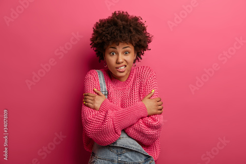 Slika na platnu Studio shot of good looking ethnic curly haired woman trembles from feeling cold