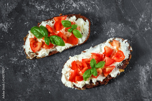 Bruschetta caprese toast with tomatoes, soft cottage cheese and basil on a dark blue background. Traditional Italian snack. Top view. Close-up