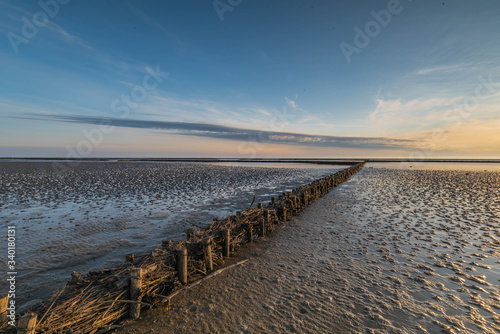 An impressive view from the dike foreland near the Büsum, Westerdeichstrich, Nordfriesland, Schleswig-Holstein Germany, wooden groyne on the beach of North Sea, sunset over the the Wadden Sea, mudflat