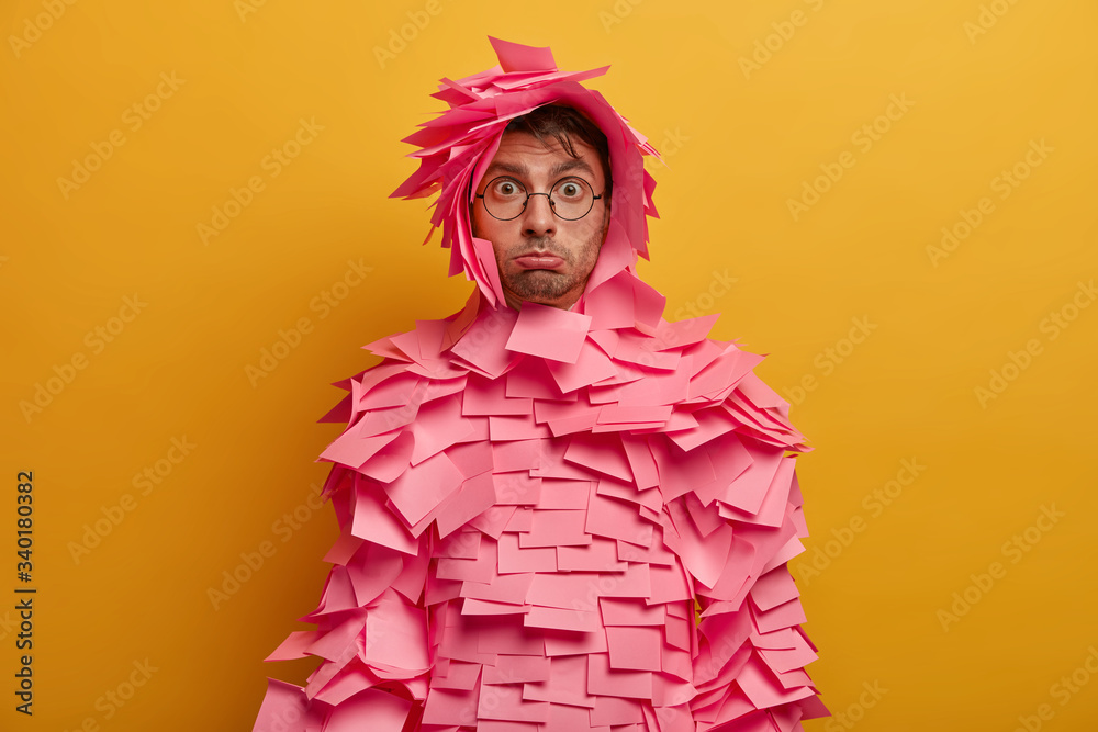 Φωτογραφία Studio shot of displeased unshaven European man feels unhappy, purses lower lip, stands offended, covered with pink sticky notes, wears spectacles, isolated on yellow background