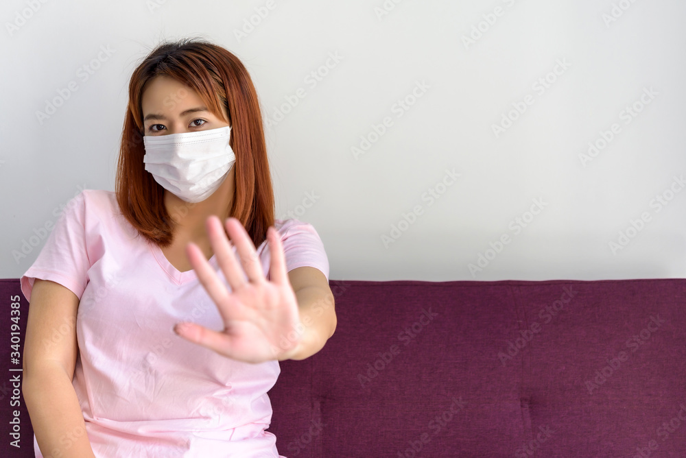 portrait of young Asian woman sitting on sofa at living room in her house and wearing face medical mask. Flu epidemic, dust allergy, protection against virus. Covid-19, corona virus pandemic portrait of young Asian woman sitting on sofa at living room in her house and wearing face medical mask. Flu epidemic, dust allergy, protection against virus. Covid-19, corona virus pandemic