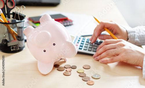 Women counting coins on calculator taking from the piggy bank. Use last savings, unemployment and bankruptcy concept. photo