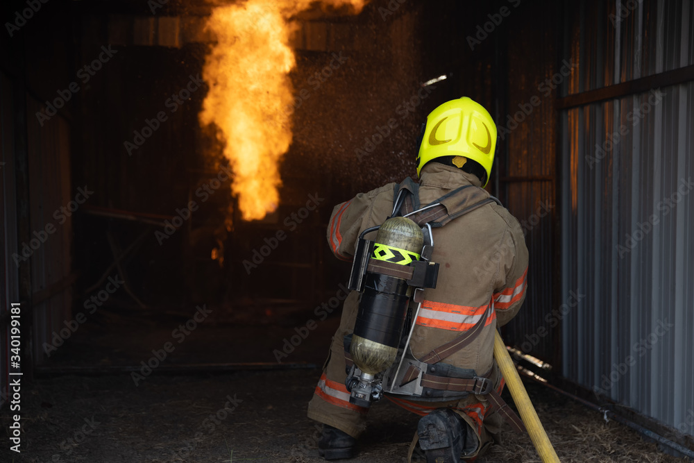 Rear view of Fireman wear fire protection suit walking into the fire training room and Spray water Fire at fire station. Training fire drill Concept. Rear view of Fireman wear fire protection suit walking into the fire training room and Spray water Fire at fire station. Training fire drill Concept.