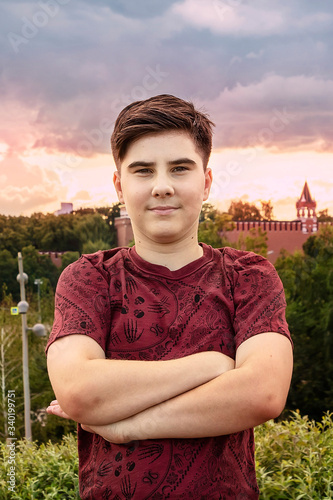 A teenager with dark hair and brown eyes stands against a sunset.