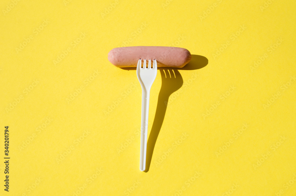 Sausage and white plastic fork on a bright yellow background with hard light Sausage and white plastic fork on a bright yellow background with hard light