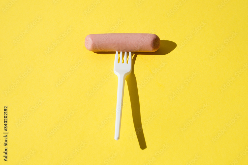 Sausage and white plastic fork on a bright yellow background with hard light Sausage and white plastic fork on a bright yellow background with hard light