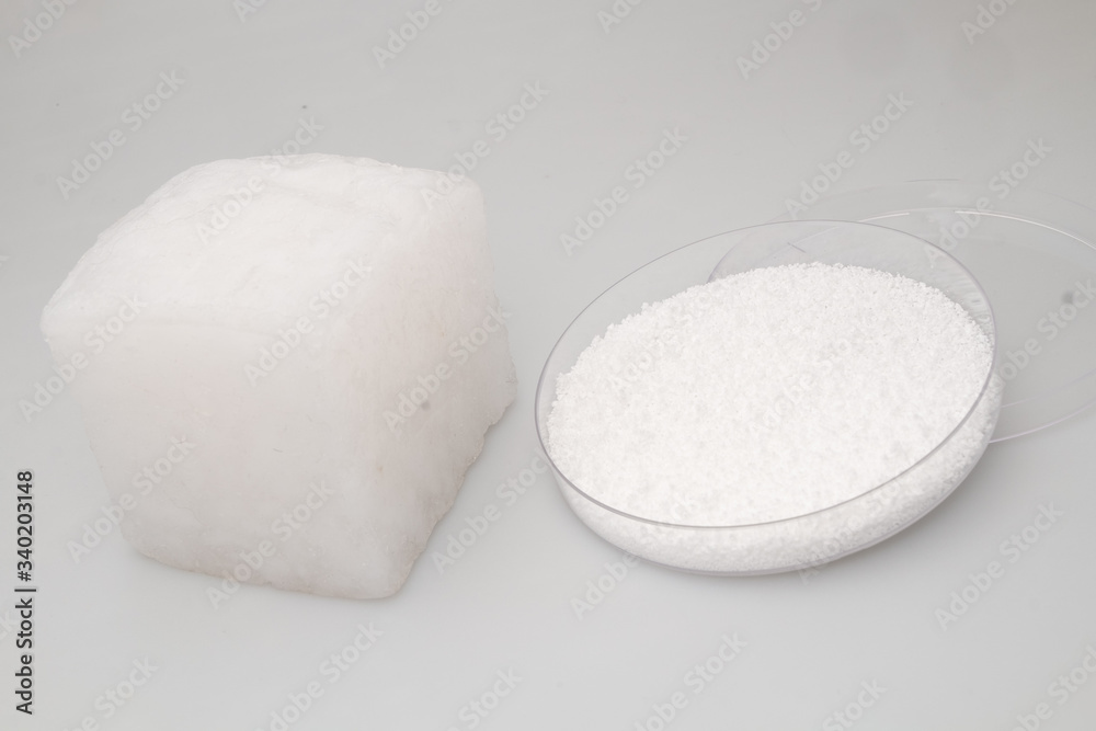 glass laboratory jar with samples of white synthetic rubber and a cube of white rubber next to it on a white background