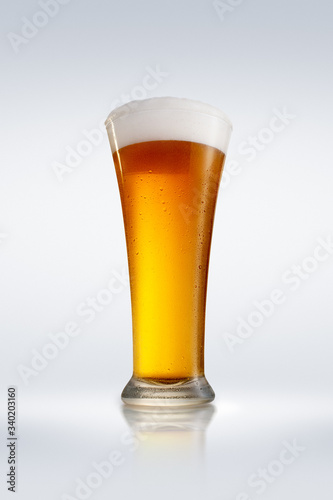 A glass of foamy beer on a glossy tabletop with bright gradient background