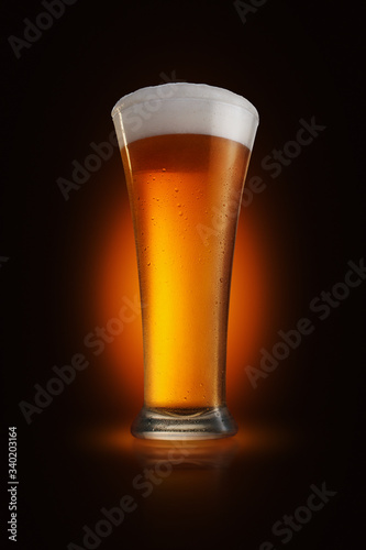 A glass of foamy beer on a glossy tabletop with dark gradient background, spotlight immitation