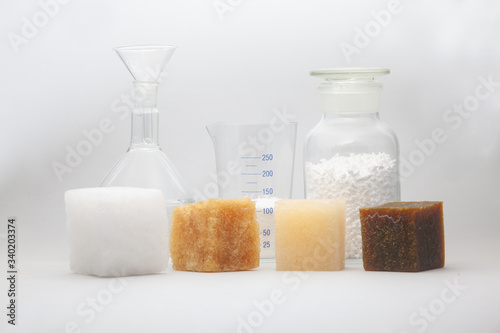 multi-colored samples of a cube of polymer synthetic rubber and laboratory glass jars in the background shot on a white background