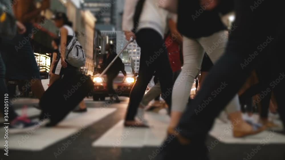Low angle slow motion shot of people's legs and feet walking across a busy city street near Times Square in the evening.