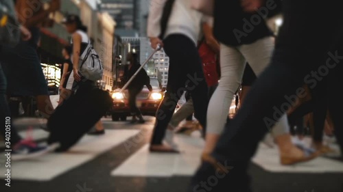 Low angle slow motion shot of people's legs and feet walking across a busy city street near Times Square in the evening.