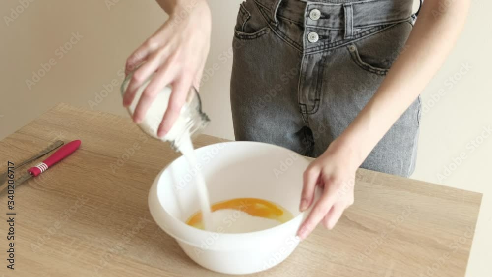 young woman in jeans and t-shirt pours sugar into dough and rolls out dough while preparing a meal young woman in jeans and t-shirt pours sugar into dough and rolls out dough while preparing a meal
