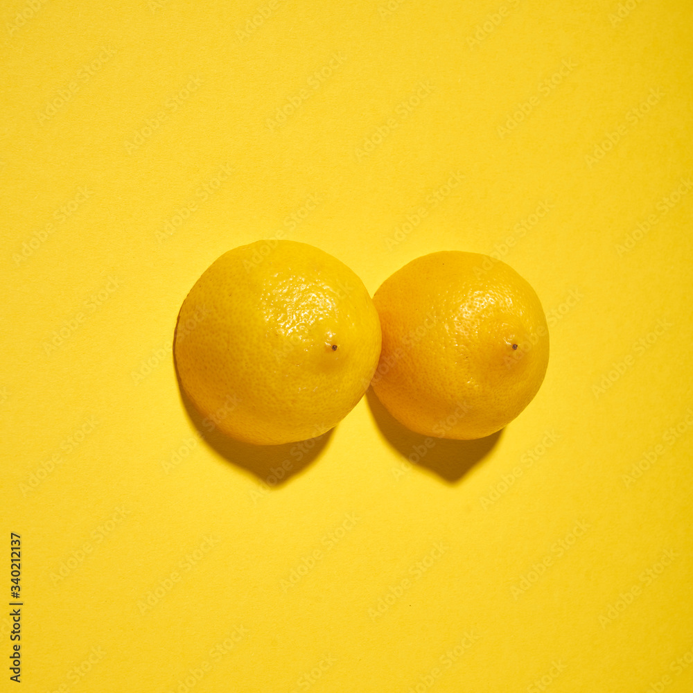 Two yellow lemons on a bright yellow background, imitation of a beautiful female breast. - obrazy, fototapety, plakaty 
