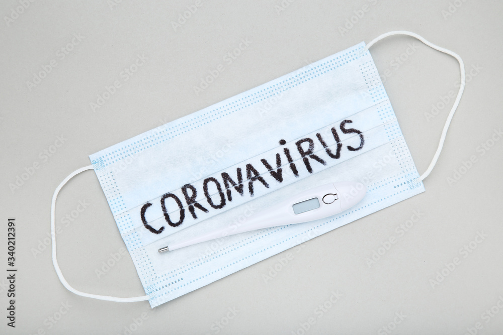 Mask with text Coronavirus and themometer on grey background Mask with text Coronavirus and themometer on grey background