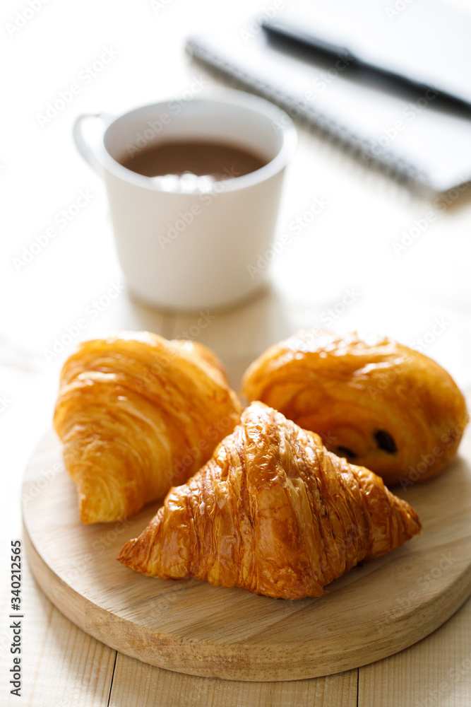 A cup of hot chocolate and croissant on wooden background with notebook. Work from home. A cup of hot chocolate and croissant on wooden background with notebook. Work from home.