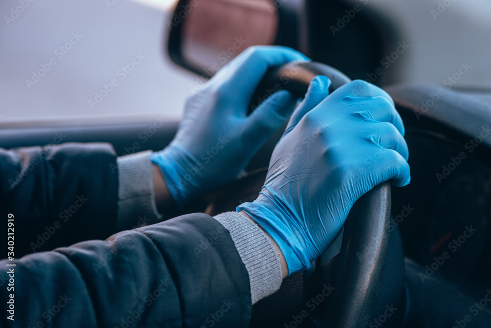 A man holds the steering wheel of a car in protective medical gloves. Hands close-up. Safe drive in a taxi during pandemic coronavirus. Protect driver and passengers from bacteria and virus infection.