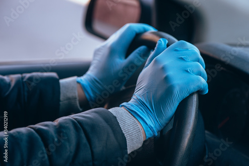 A man holds the steering wheel of a car in protective medical gloves. Hands close-up. Safe drive in a taxi during pandemic coronavirus. Protect driver and passengers from bacteria and virus infection. © blinova