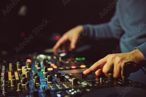 hands of dj are mixing tracks at party in night club. disc jockey playing music on the modern turntable close up. 