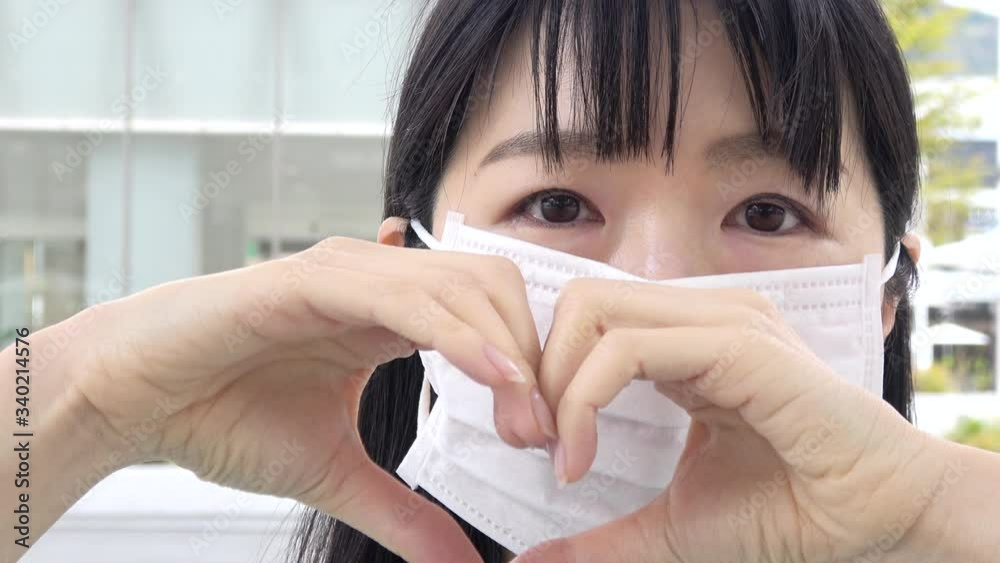 Young Asian woman with a surgical mask forming a heart shape with hands. Closeup shot. 4K Young Asian woman with a surgical mask forming a heart shape with hands. Closeup shot. 4K