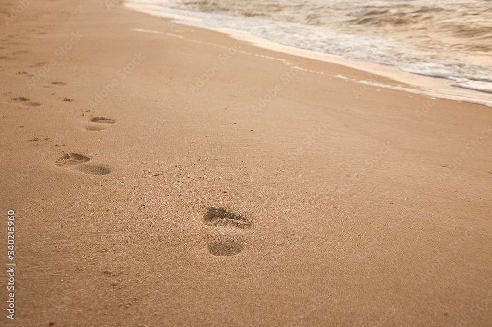 Natural background for text and sand and sea waves. Footprints in the sand from the legs go into the distance. Summer, sea, sunrise. Natural background for text and sand and sea waves. Footprints in the sand from the legs go into the distance. Summer, sea, sunrise.