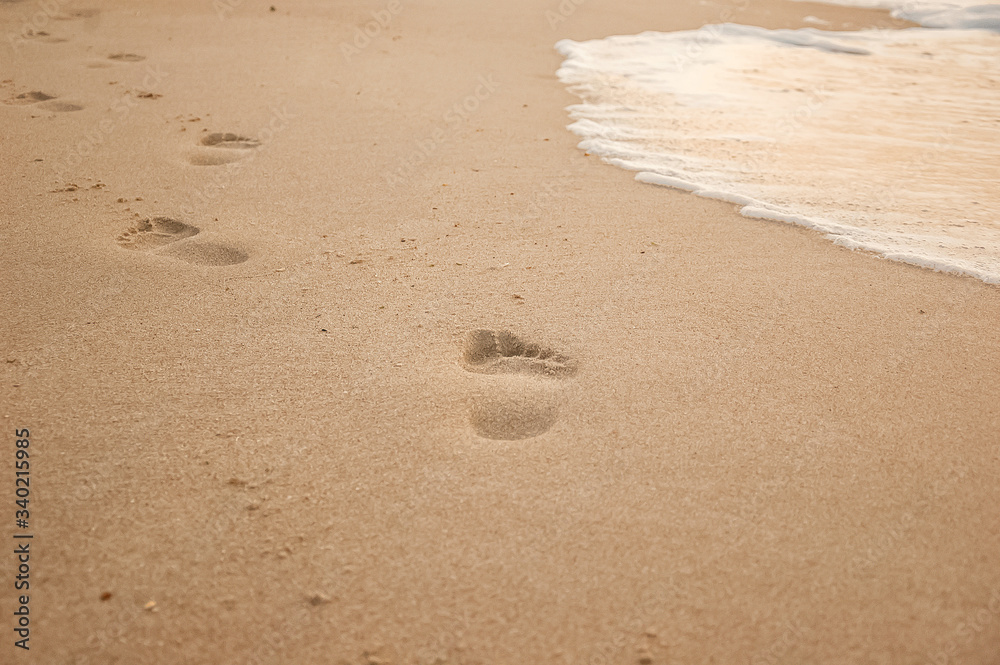 Natural background for text and sand and sea waves. Footprints in the sand from the legs go into the distance. Summer, sea, sunrise. Natural background for text and sand and sea waves. Footprints in the sand from the legs go into the distance. Summer, sea, sunrise.