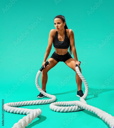Sweaty woman resting after working out with ropes. Photo of sporty woman on turquoise background. Strength and motivation. Full length © Romario Ien