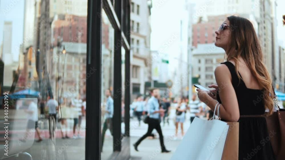 Young beautiful woman using the smartphone near the shop-window and than turning, walking away. Slow motion.