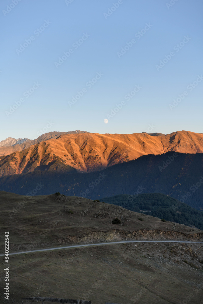 The moon rises over a mountain lit by the setting sun in the Tusheti region.