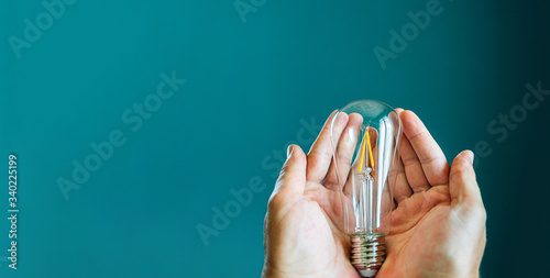 Two hands holding a light bulb on a green background