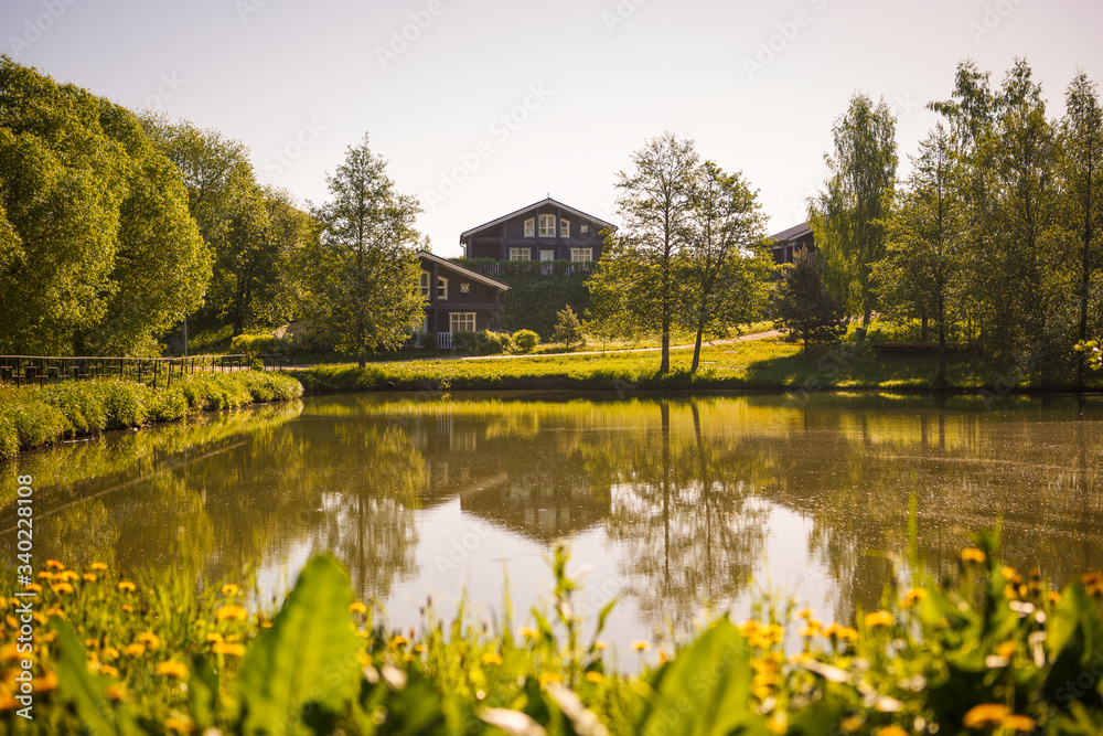 Lake in the Park among green trees and fields of dandelions. Trees are reflected in the lake and two wooden boats are standing on the shore Lake in the Park among green trees and fields of dandelions. Trees are reflected in the lake and two wooden boats are standing on the shore