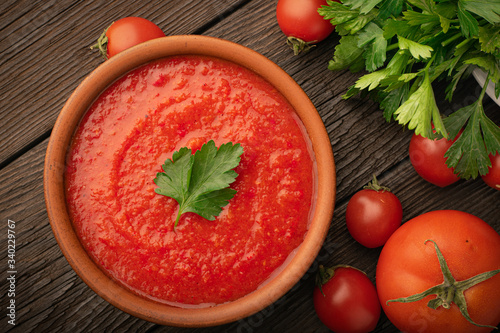 Top view bowl of tomato soup and fresh tomatoes with parsley on a wooden background