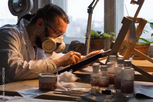 The master restorer in a white coat and respirator restores the icon, the restorer works in his restoration workshop
