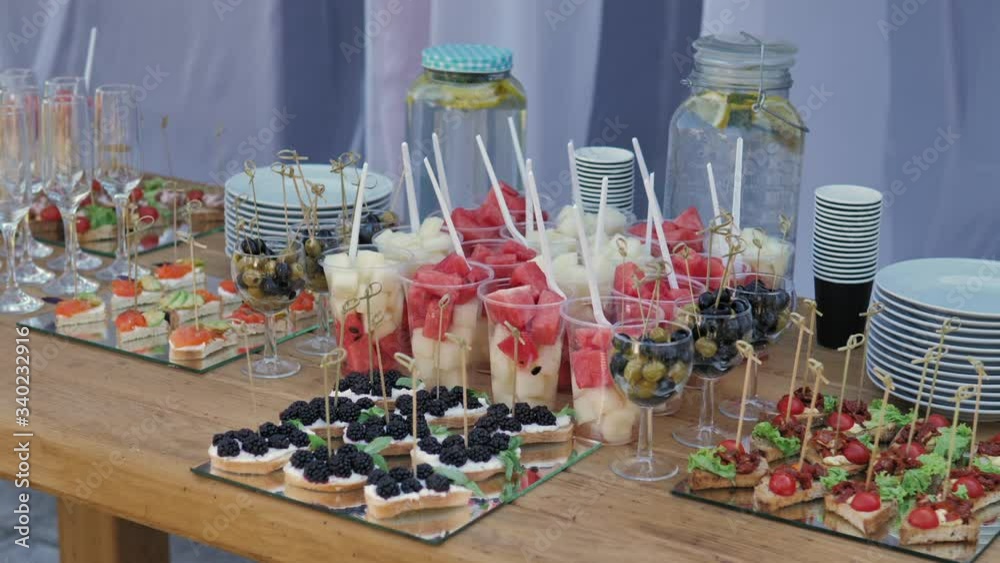 Buffet table with snacks, canape, fruits and limonade at wedding reception. Serving food and drinks at event. Catering banquet table. Reception, snacks outdoor. 