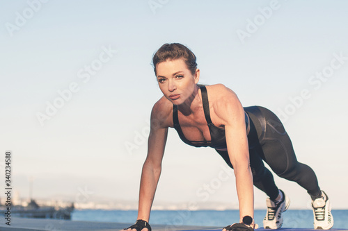Caucasian female fitness model performing upper plank fitness exercise outdoor at sea promenade