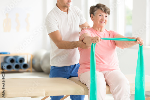 Senior exercising with an resistance band with a support of a physiotherapist