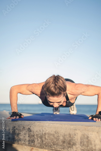 Caucasian female fitness model performing push up exercise outdoor at sea promenade