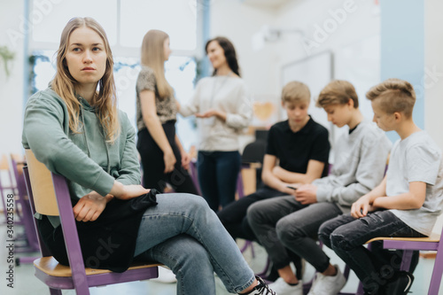 Pretty thoughtful teenage girl sits on the side of a group during extracurricular activities at school