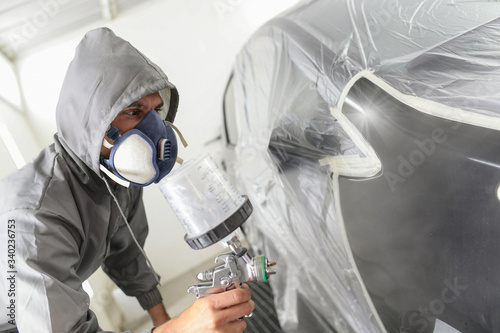 Car body worker paints a car in the paint booth with a spraying paint