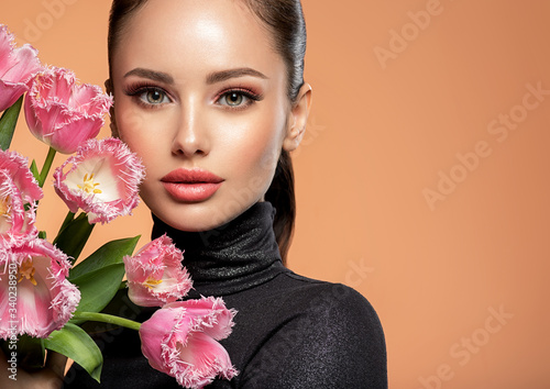 Beautiful white girl with flowers. Stunning brunette girl with big bouquet flowers of pink tulips. Pretty woman with bright makeup