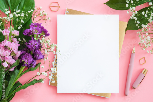 Blank white sheet on spiral golden notepad with pen for your text or design and bouquet of flowers on pink background. Concept Female workspace Mockup Top view Flat lay