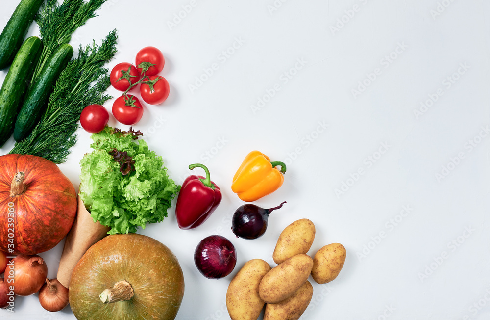 Groceries: two pumpkins, potatoes, sprig of tomatoes, onions, red and yellow bell peppers, cucumbers, dill, lettuce on white background, packed on the left Groceries: two pumpkins, potatoes, sprig of tomatoes, onions, red and yellow bell peppers, cucumbers, dill, lettuce on white background, packed on the left